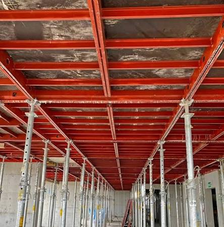 Red modular slab shoring system supporting elevated deck formwork from below