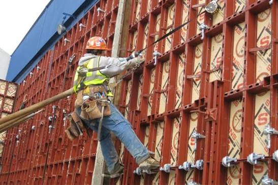 Worker installing light clamp forming panels on a tall concrete wall